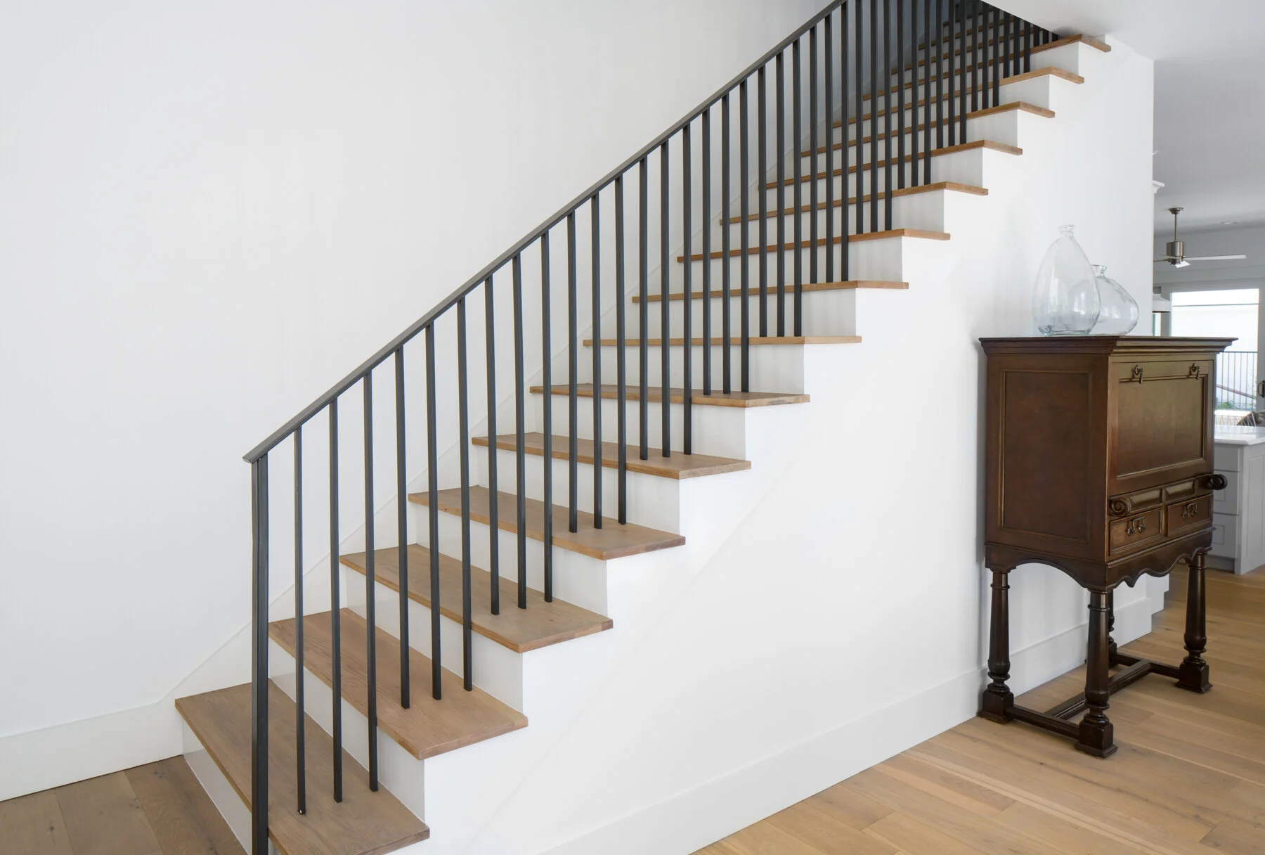 Side-by-side comparison: a dark oak staircase with a curved twisted-iron railing before renovation, next to the same style of staircase after renovation with light oak treads and a scrollwork iron railing pattern